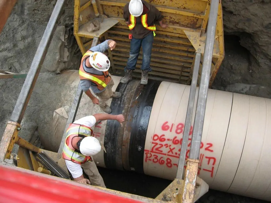 Workers inspecting large underground pipeline installation.