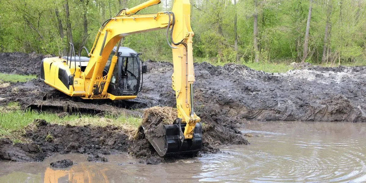 Excavator digging near a muddy water area.